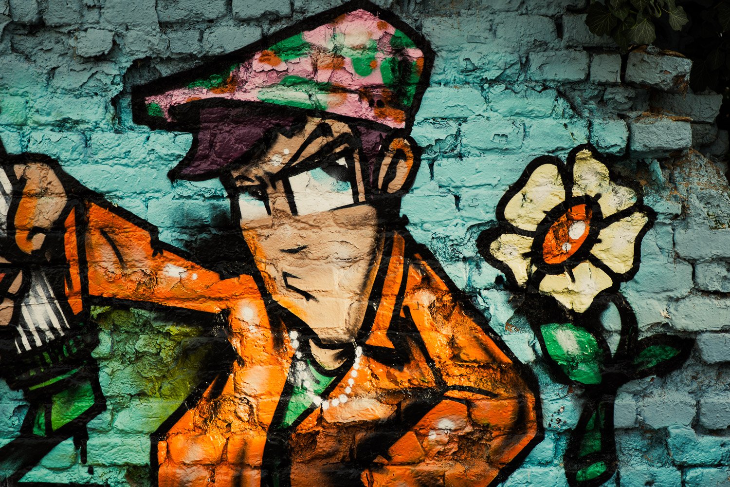 Close-up of vibrant street art in Zagreb featuring a character wearing an orange jacket, floral hat, and face covering, painted on a textured blue brick wall.